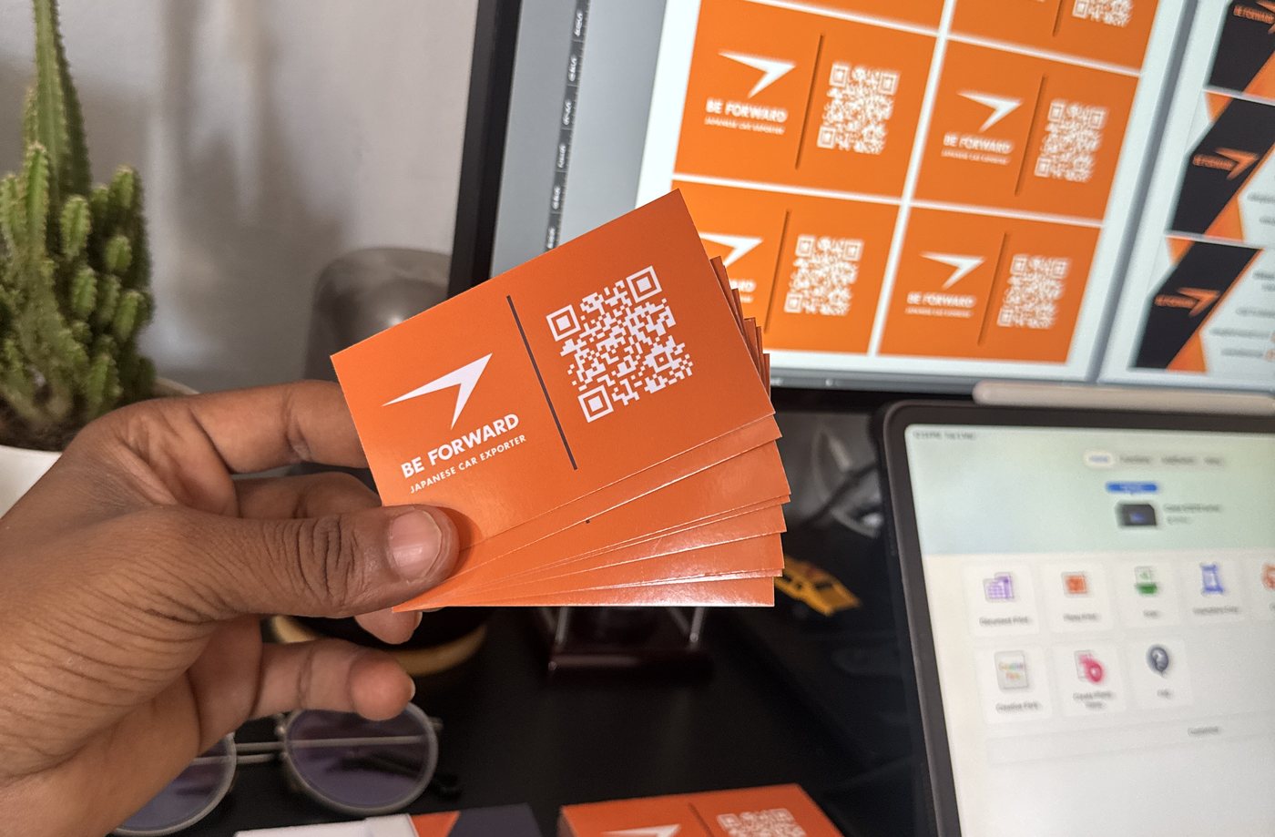 Printed BE FORWARD business cards held in hand beside the artwork on screen